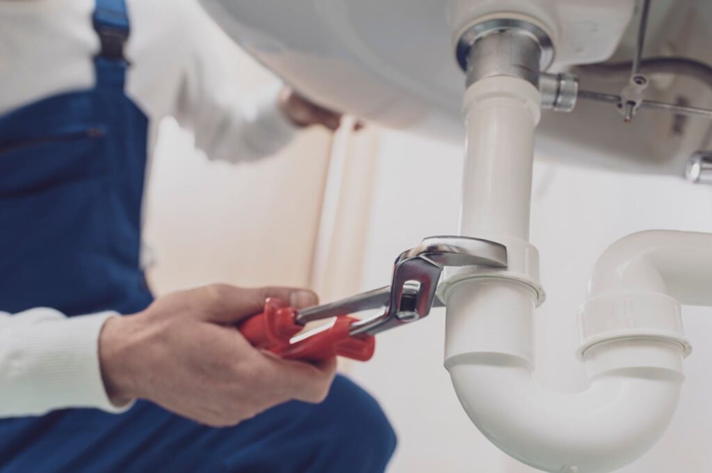 Plumber repairing a white drain pipe beneath a sink in Brighton