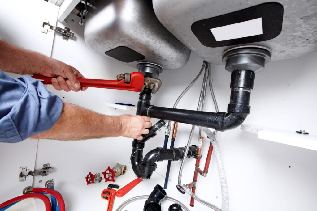 Plumber repairing drain pipes beneath a kitchen sink in Brighton