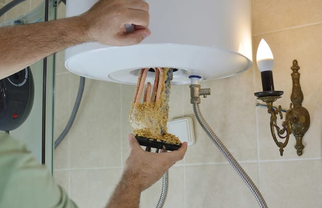 Technician removing mineral buildup from a water heater in Brighton