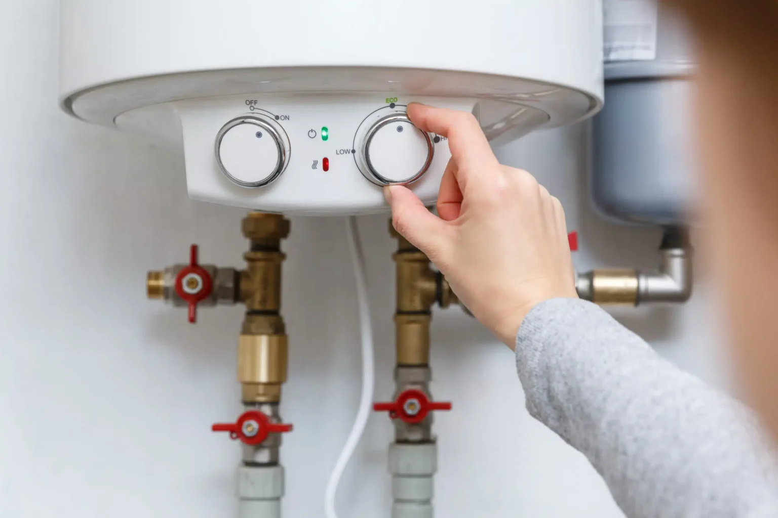 Homeowner adjusting the temperature controls on a water heater in Brighton